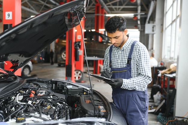 Indian car mechanic standing and working in service station Car specialists examining the lifted car Professional repairmen wearing mechanic uniform in blue color