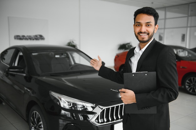 Indian cheerful car salesman showing new car at showroom