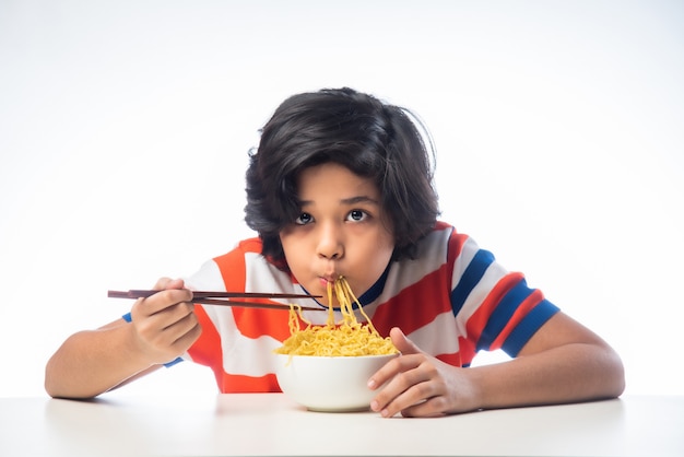 Indian child eating delicious noodles with Fork against White Background,ÃÂ  Asian boy eats Spaghetti in a bowl against white background