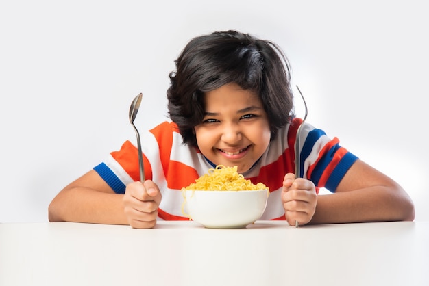 Indian child eating delicious noodles with Fork against White Background,ÃÂ  Asian boy eats Spaghetti in a bowl against white background