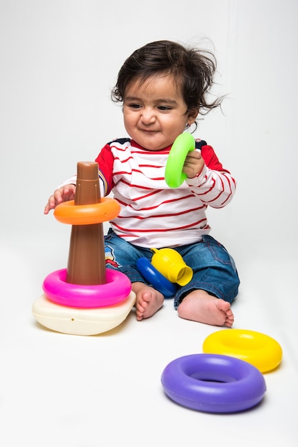 Indian cute little baby or infant or toddler playing with toys or blocks over white background,