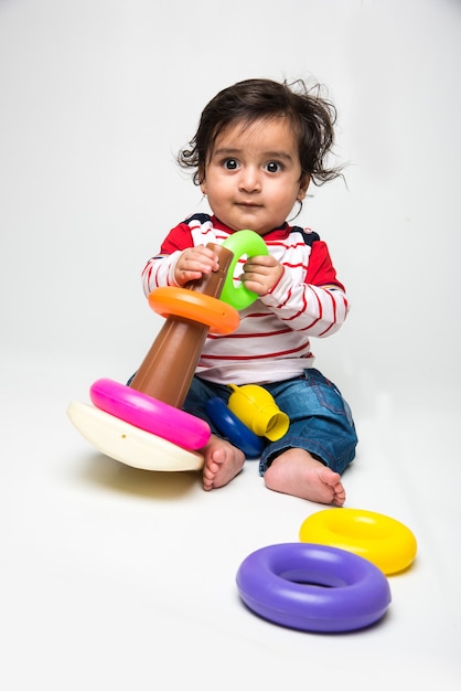 Indian cute little baby or infant or toddler playing with toys or blocks over white background,