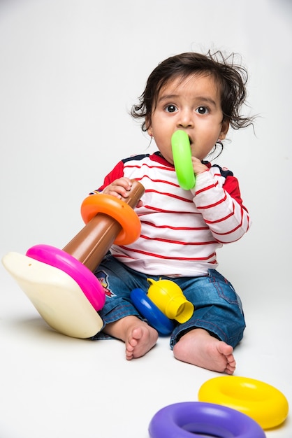 Indian cute little baby or infant or toddler playing with toys or blocks over white background,