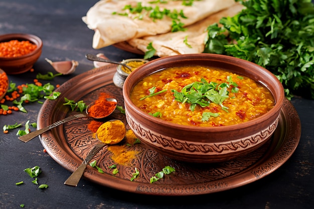 Indian Dhal spicy curry in bowl, spices, herbs, rustic black wooden background.