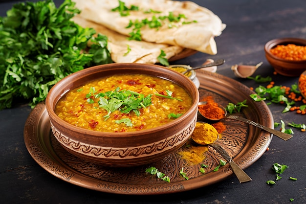 Indian Dhal spicy curry in bowl, spices, herbs, rustic black wooden background.