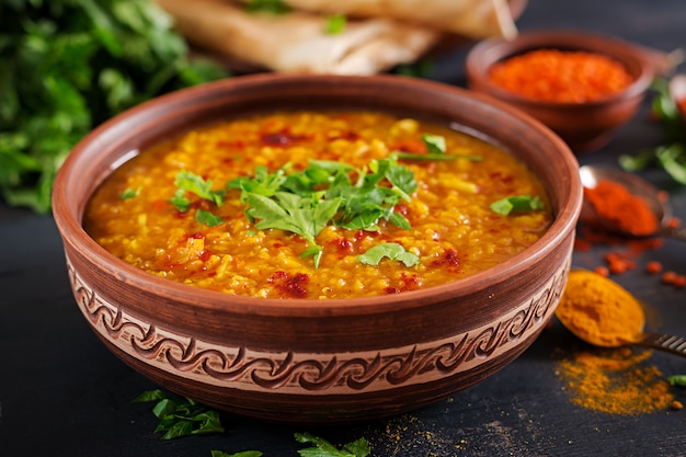 Indian Dhal spicy curry in bowl, spices, herbs, rustic black wooden background.