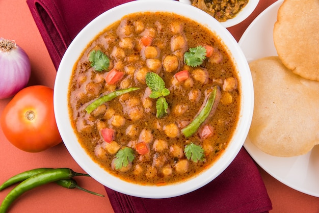 Photo indian dish spicy chick peas curry also known as chola or chana masala or commonly chole, served served with fried puri or poori over colourful or wooden background. selective focus