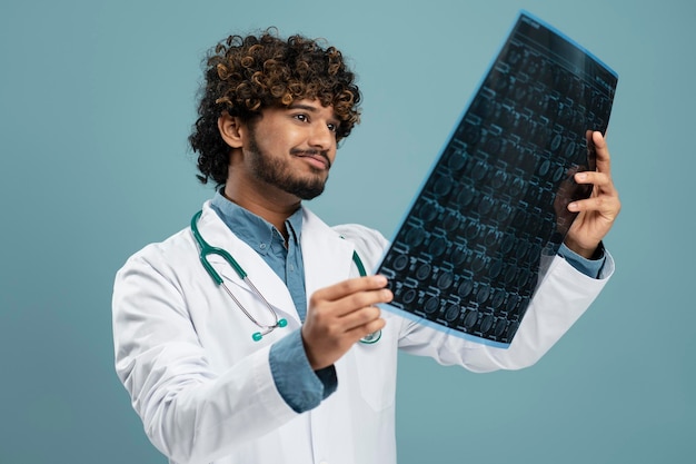 Indian doctor with stethoscope wearing white lab coat, holding roentgen or x ray in hospital