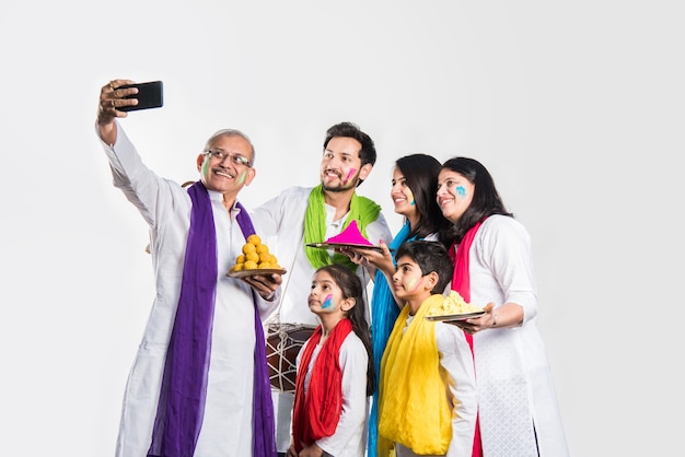 Indian family celebrating holi festival with sweet laddu gifts and colours in plate. isolated over white background. selective focus meaning