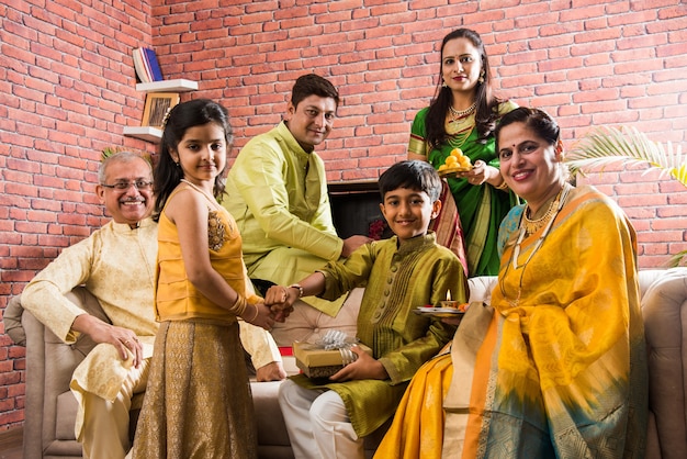 Indian Family celebrating Raksha Bandhan or Rakhi festival at home while wearing traditional cloths and sitting over sofa