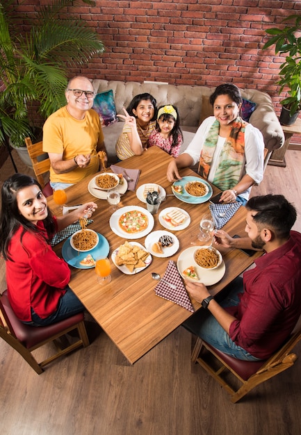 Indian Family eating food at dining table at home or restaurant having meal together