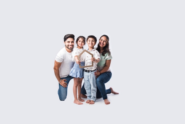 Indian family Father, mother, son and daughter holding 3D paper model of home - Real Istate Concept in India