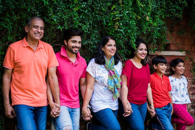 Indian family standing in line against wall covered with creepers. Multi generation of asian family in park or garden having fun, healthy family life concept