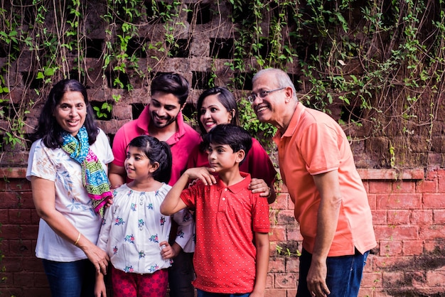 Indian family standing in line against wall covered with creepers. Multi generation of asian family in park or garden having fun, healthy family life concept