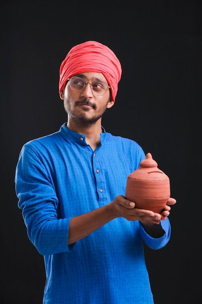 Indian Farmer holding piggy bank on dark background.