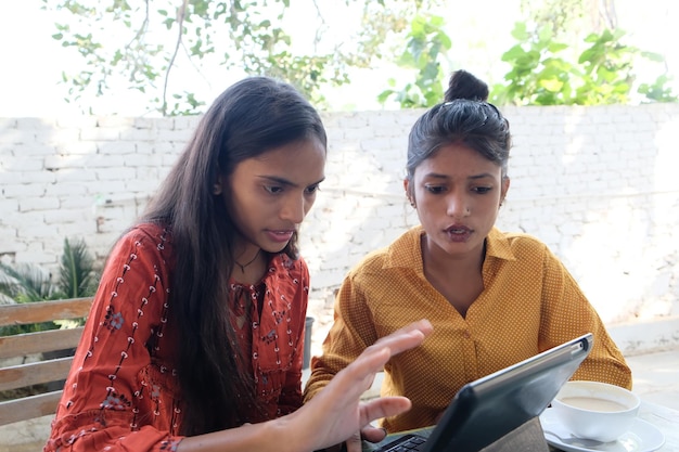 Indian female friends watching something or working on a tablet outdoors