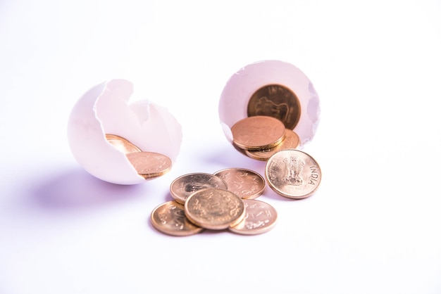 Indian five rupee golden coins emerging from cracked egg, isolated over white background