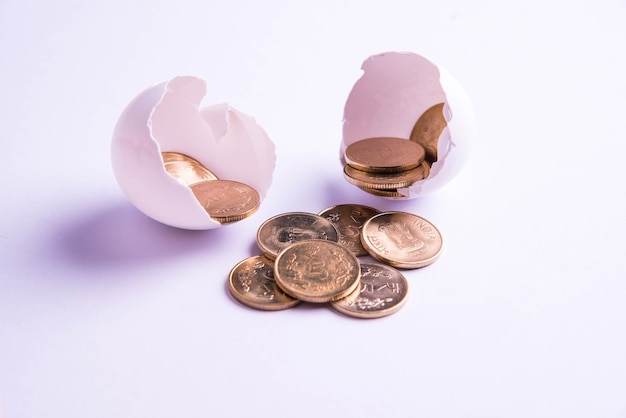 Indian five rupee golden coins emerging from cracked egg, isolated over white background