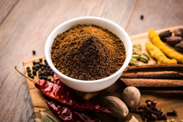 Indian Garam masala powder in bowl and it's ingredients colourful spices. Served over moody background. selective focus