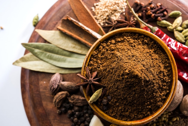 Indian Garam masala powder in bowl and it's ingredients colourful spices. Served over moody background. selective focus