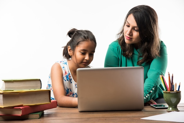 Indian girl studying with mother or teacher at study table with laptop computer, books and having fun learning