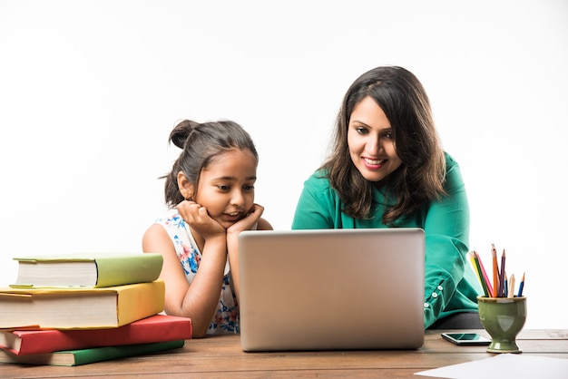 Indian girl studying with mother or teacher at study table with laptop computer, books and having fun learning