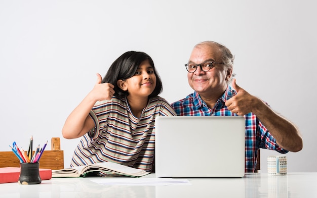 Indian grandfather teaching granddaughter with books, pencil and laptop, home schooling or tuition