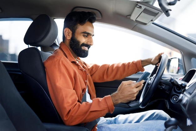 Indian guy using smartphone messaging while driving car side view