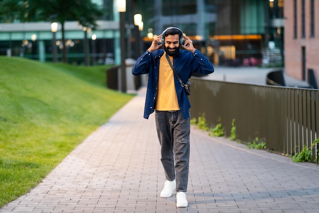 Indian guy wearing headphones enjoying walk with favorite music outdoor