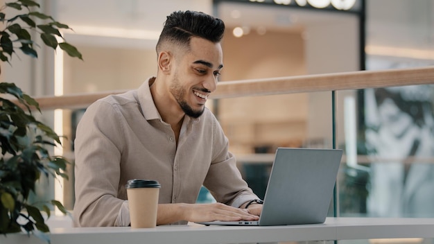 Indian hispanic ethnic businessman male worker guy man in cafe with laptop happy with luck fortune