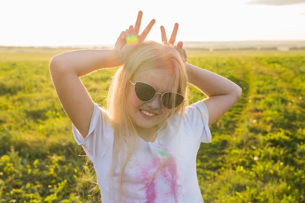 Indian holidays, fun and childhood concept - girl in glasses smiling, having fun on the holi festival.