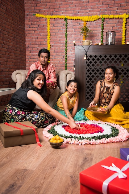 Indian Kids celebrating Diwali, Deepawali, Bhai Dooj or Rakhi or Raksha Bandhan with flower rangoli, gifts, diya