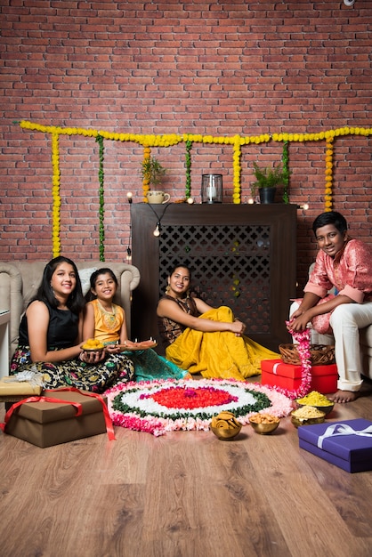 Indian Kids celebrating Diwali, Deepawali, Bhai Dooj or Rakhi or Raksha Bandhan with flower rangoli, gifts, diya