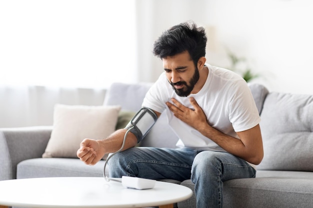 Indian man feeling unwell at home checking blood pressure with arm monitor