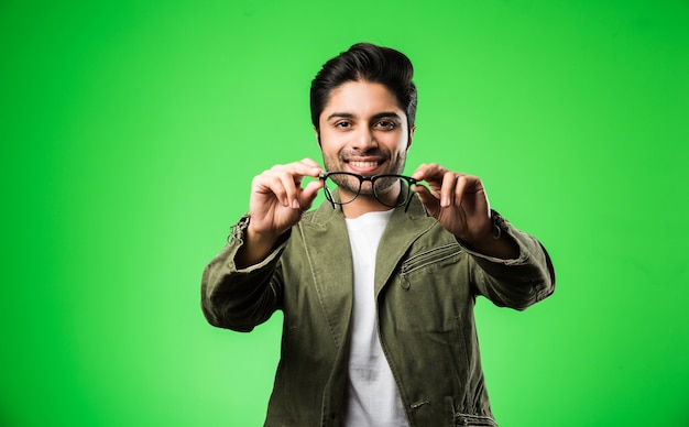 Indian man showing eye glasses, wearing t-shirt and jacket, standing isolated