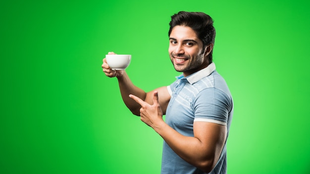 Indian man with tea or coffee cup or mug. Drinking, presenting or holding while standing isolated