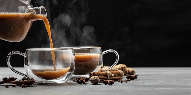 Indian masala chai tea Hot masala chai spiced tea with milk and spices is poured into a glass glass on dark background Long banner format place for text