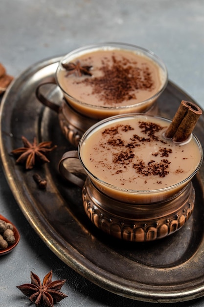 Indian masala chai tea Hot masala chai spiced tea with milk and spices is poured into a glass glass on dark background vertical image place for text