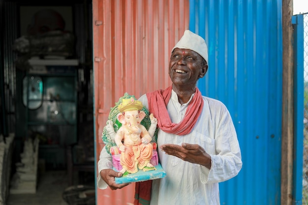 Indian old man holding Lord Ganesha idol in hands happy old poor man