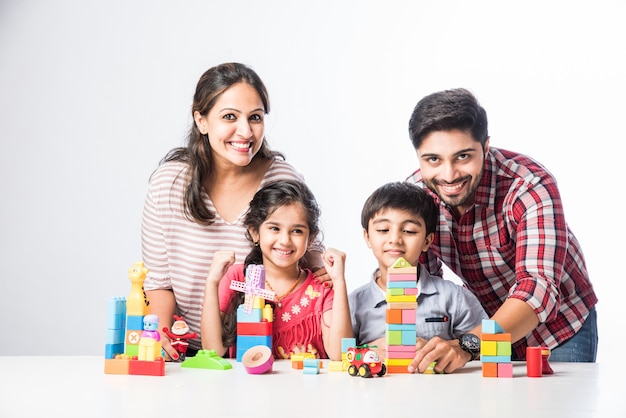 Indian small kids playing colourful block toys with young parents, against white background