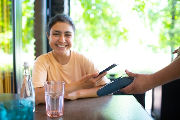 Indian Woman pay with mobile phone nfc contactless payment terminal in cafe bar.