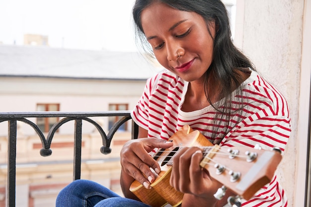 Indian woman playing ukulele on windowsill