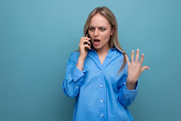 Indignant cute blonde woman chatting on the phone on a blue bright background