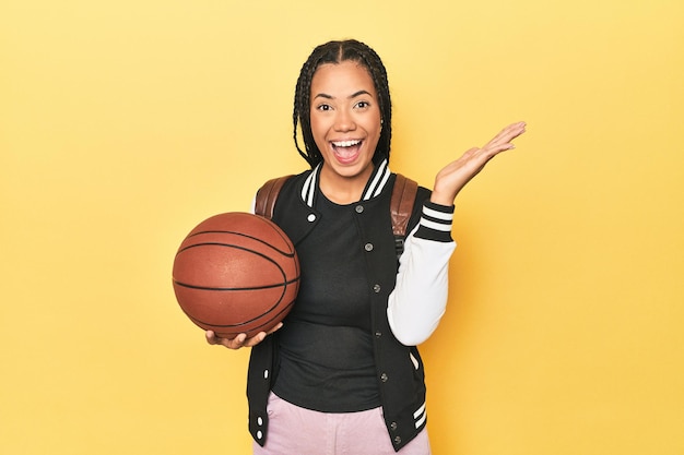 Indonesian schoolgirl with basketball on yellow receiving a pleasant surprise excited