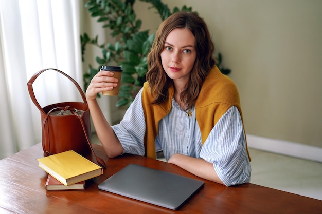 Indoor home office portrait of trendy blogge influencer working on her laptop, stylish clothes, minimalistic interior.