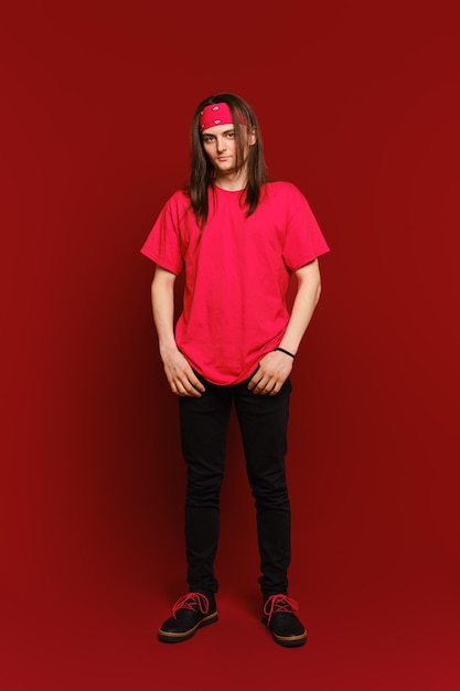 Indoor portrait of positive goodlooking hipster guy wearing red band on head standing against red wall