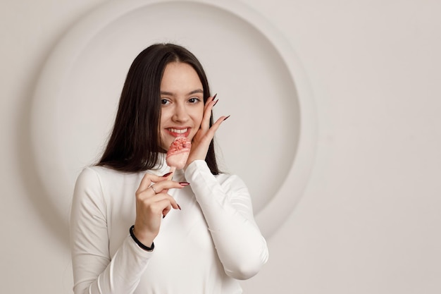 Indoor portrait of positive smiling brunette young woman on white background holding sweet dessert cake in hands