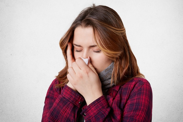 Indoor shot of female with fever and headache, uses tissue and sneezes all time, has running nose and migraine, caught seasonal virus