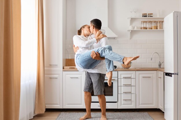 Indoor shot of loving couple posing in kitchen man holding his second part in hands and kissing her expressing romantic feelings and love couple having good time together