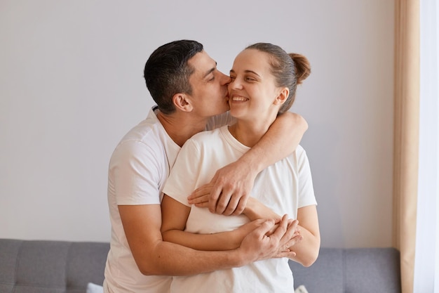 Indoor shot of young attractive couple hugging and kissing expressing happiness gentle and love being happy to spend time together posing indoor at home